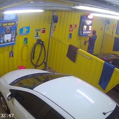 ช่องล้าง P Selfwash ระหว่างใช้งานจริง ลูกค้ายืนหันหลังกำลังใช้ตู้ควบคุม CAR WASH (P Selfwash bay during operation, customer back-turned at the CAR WASH control terminal)